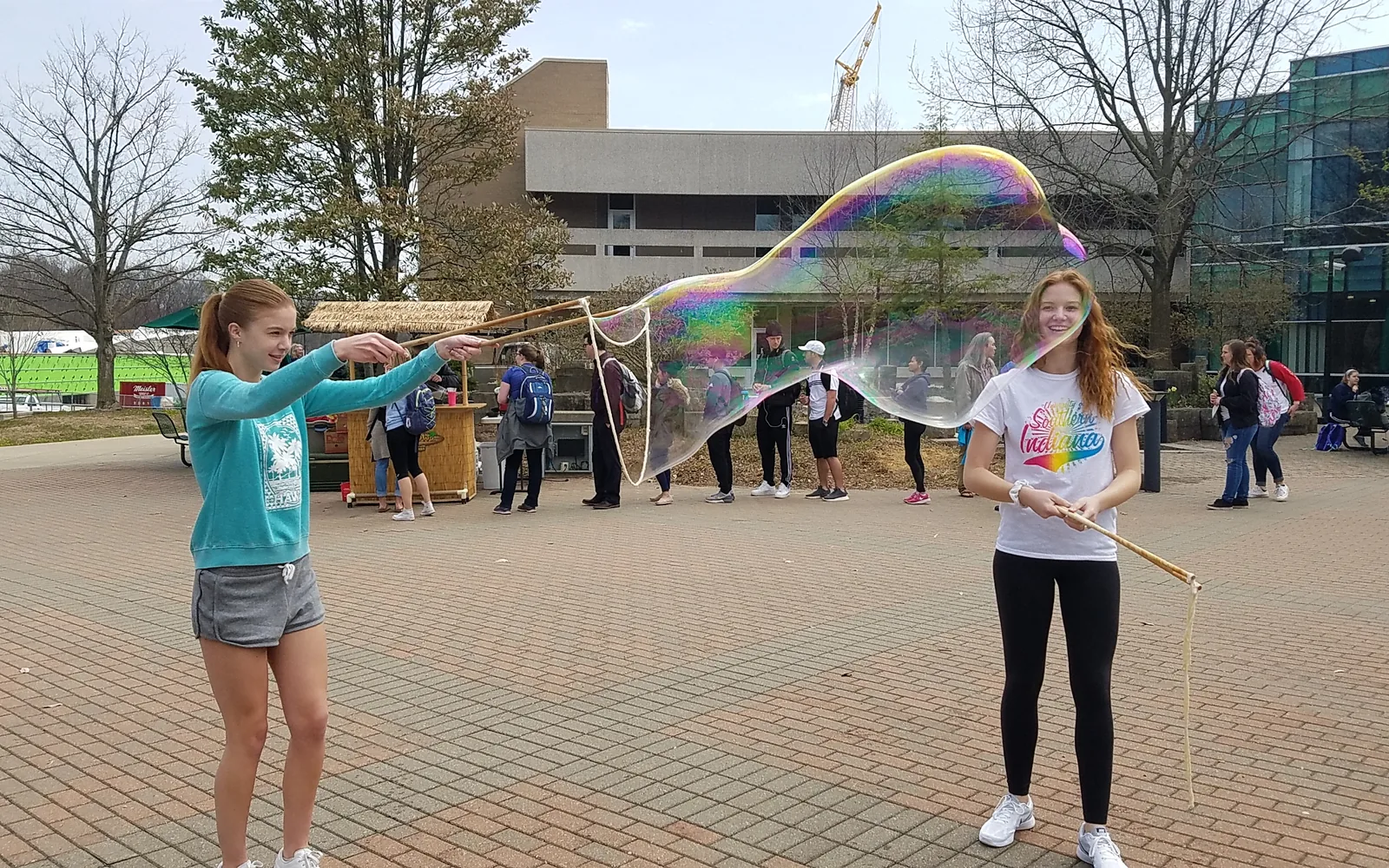 Two friends laughing as they stretch an enormous iridescent giant bubble between them with BubbleStix
