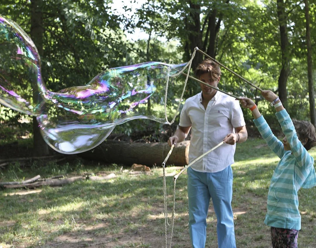 Family giant bubble making with a BubbleStix kit A father and daughter making a giant rainbow bubble together in the woods with BubbleStix