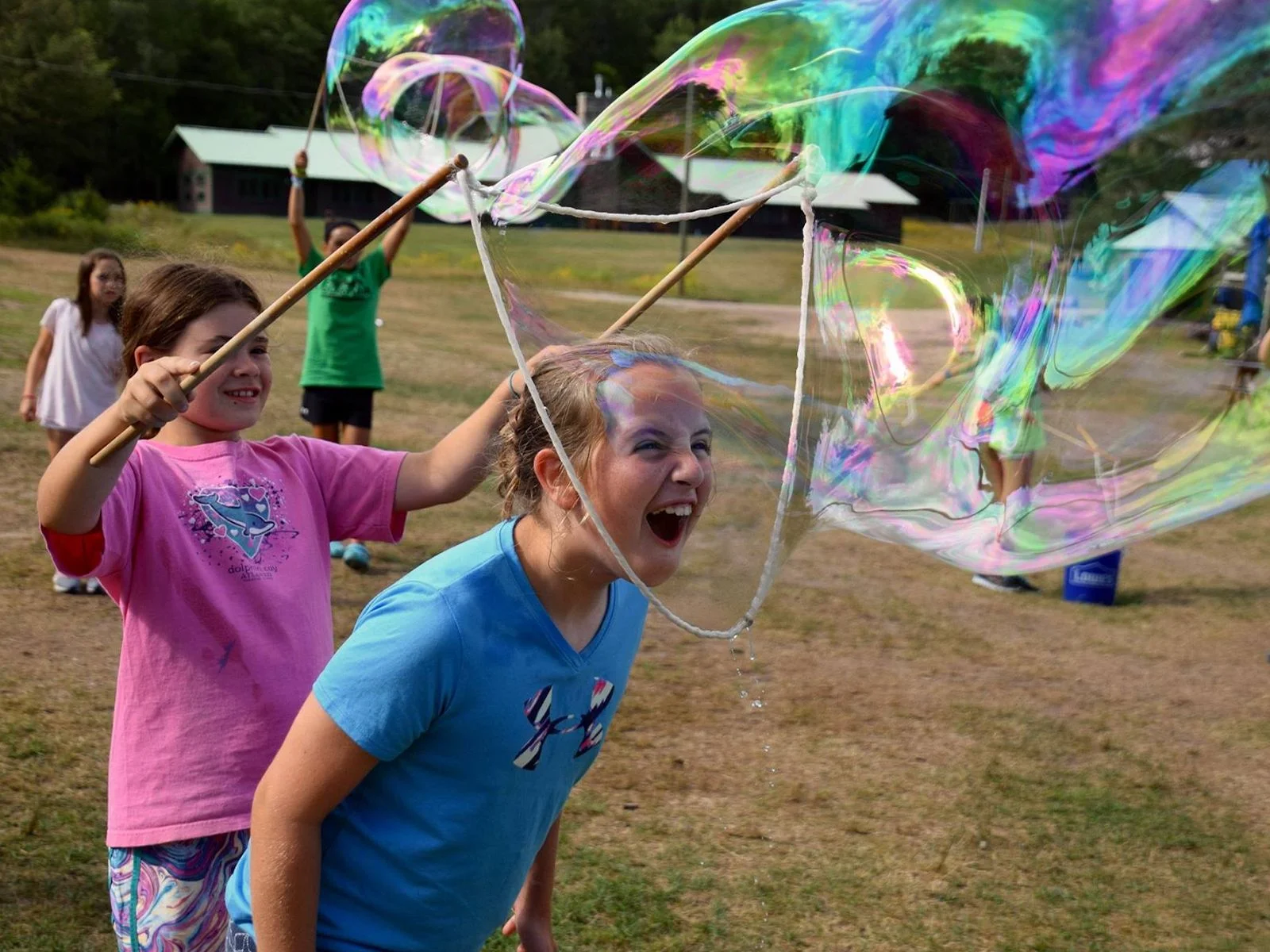 Two girls playing with giant bubbles at summer camp Two girls laughing as they make giant iridescent bubbles together at summer camp with BubbleStix