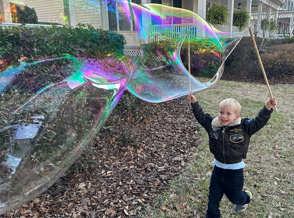 Non-toxic giant bubble formula, safe for young children A toddler reaching for a giant iridescent bubble made with BubbleStix