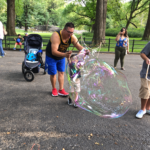 Dad and young child making a giant bubble together with a BubbleStix kit in the park