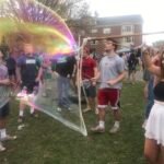 College students watching a giant bubble float past at an outdoor BubbleStix group event