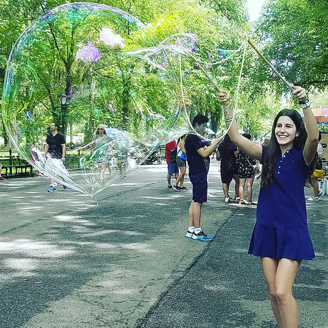 Woman in blue making a giant bubble outdoors with BubbleStix